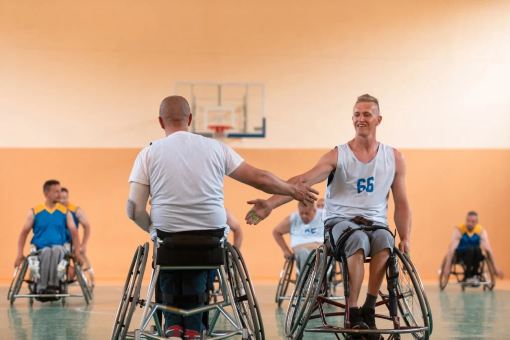 Two disabled friends in wheelchairs tapping hands in basketball game