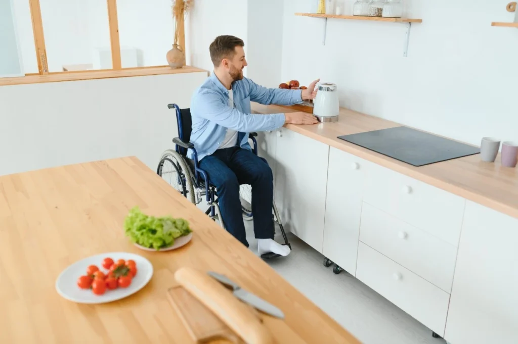 Disabled man in wheelchair putting the kettle on at home in the kitchen