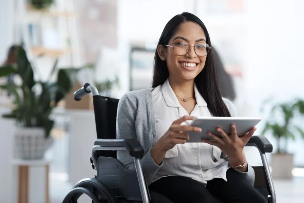 Happy disabled woman in wheelchair smiling at camera while holding iPad